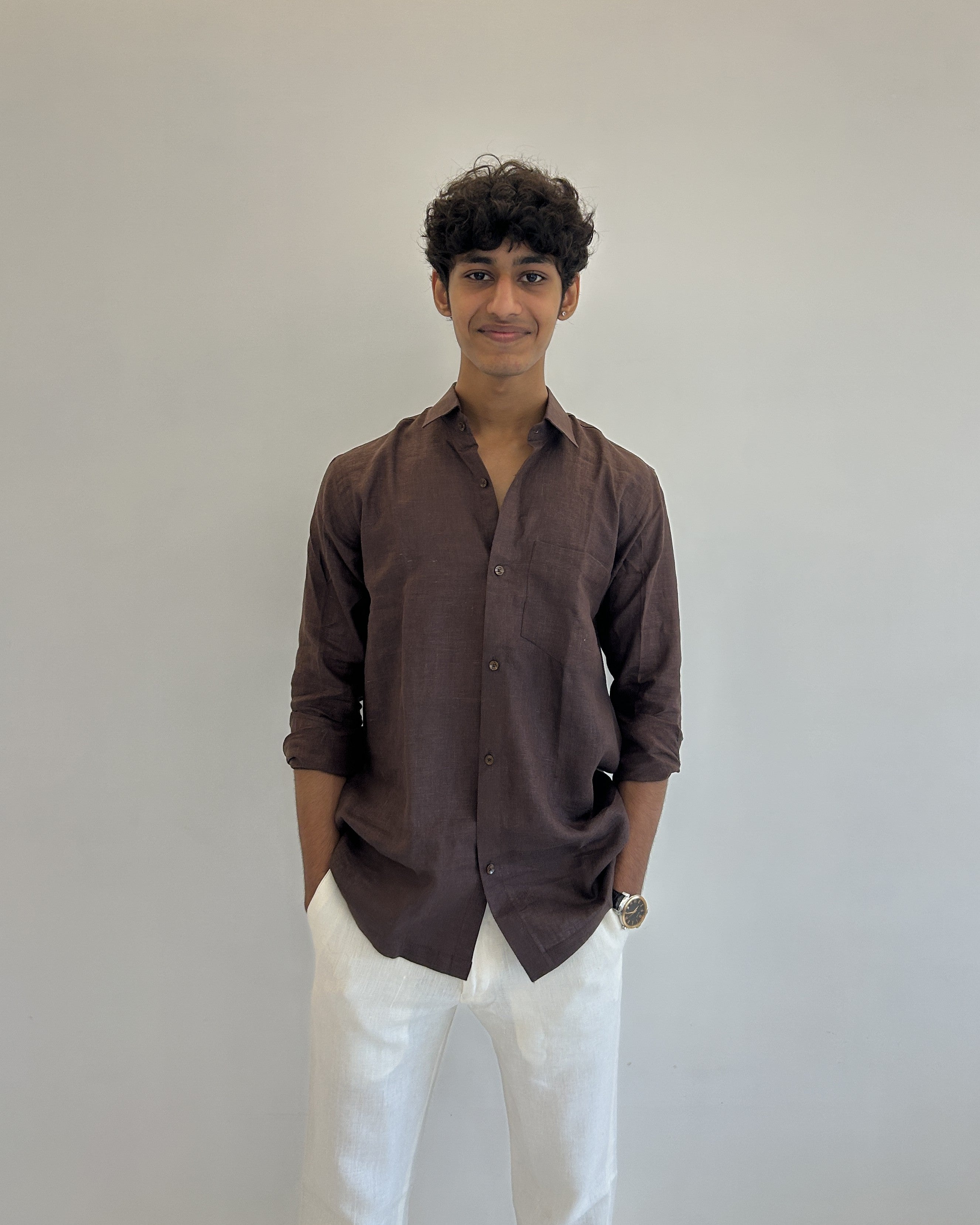 Person wearing a brown linen shirt and white pants against a plain background
