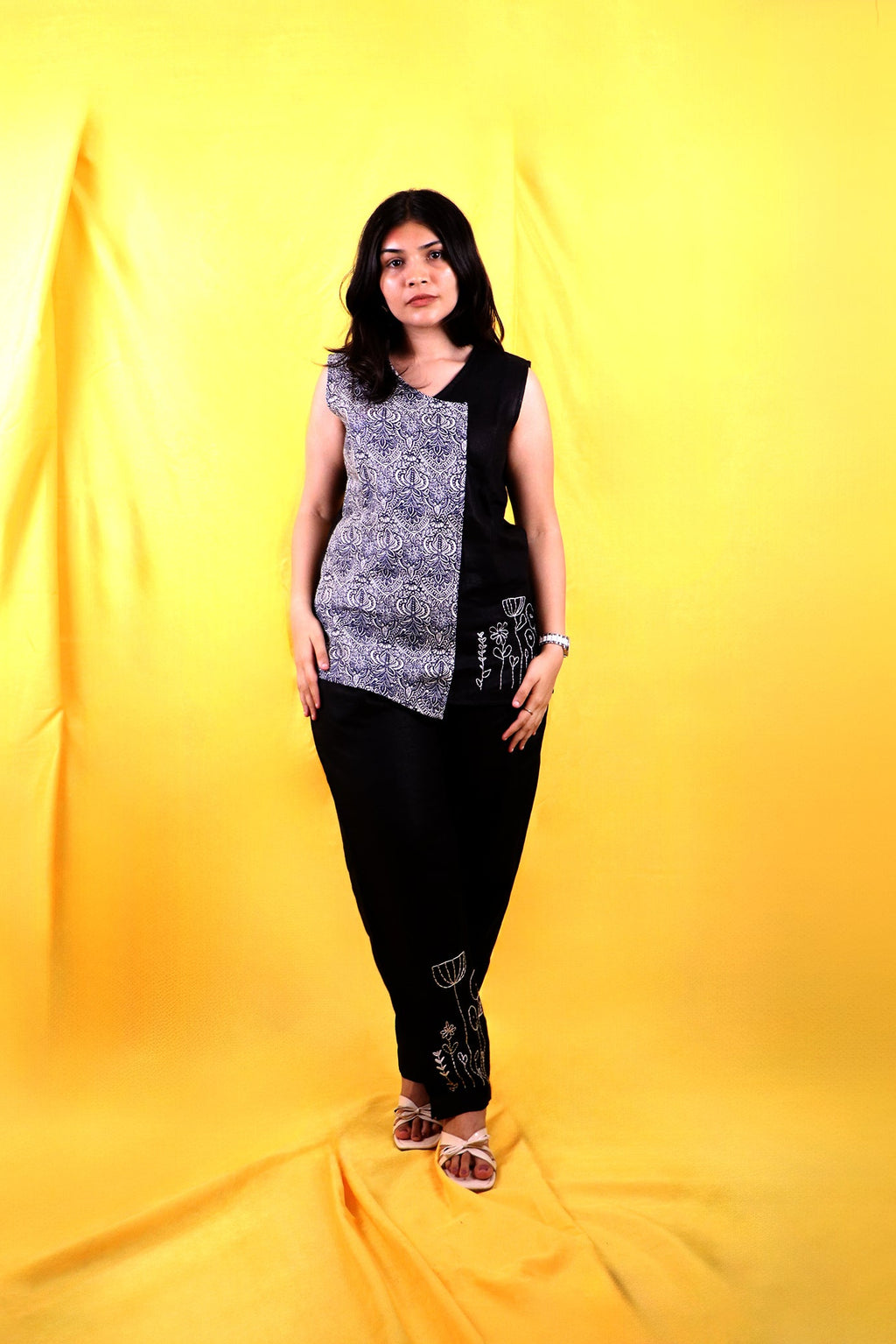 A woman wearing a black and white patterned linen top with black pants on a yellow background