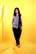 A woman wearing a black and white patterned linen top with black pants on a yellow background