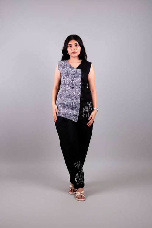 A woman wearing a black and white patterned linen top with black pants on a yellow background