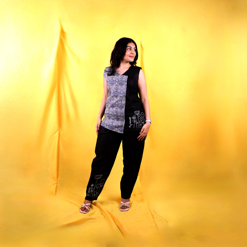 Woman wearing a black and white sleeveless linen top with black linen pants on a yellow background