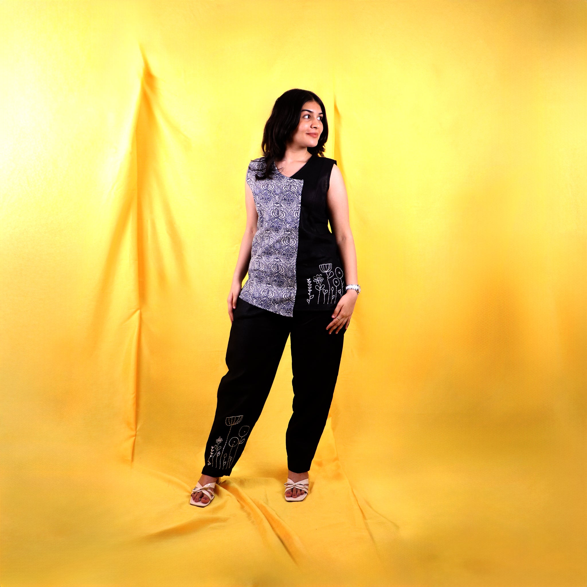Woman wearing a black and white sleeveless linen top with black linen pants on a yellow background