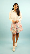 Woman wearing a light-colored shirt and a colorful skirt on a light blue background
