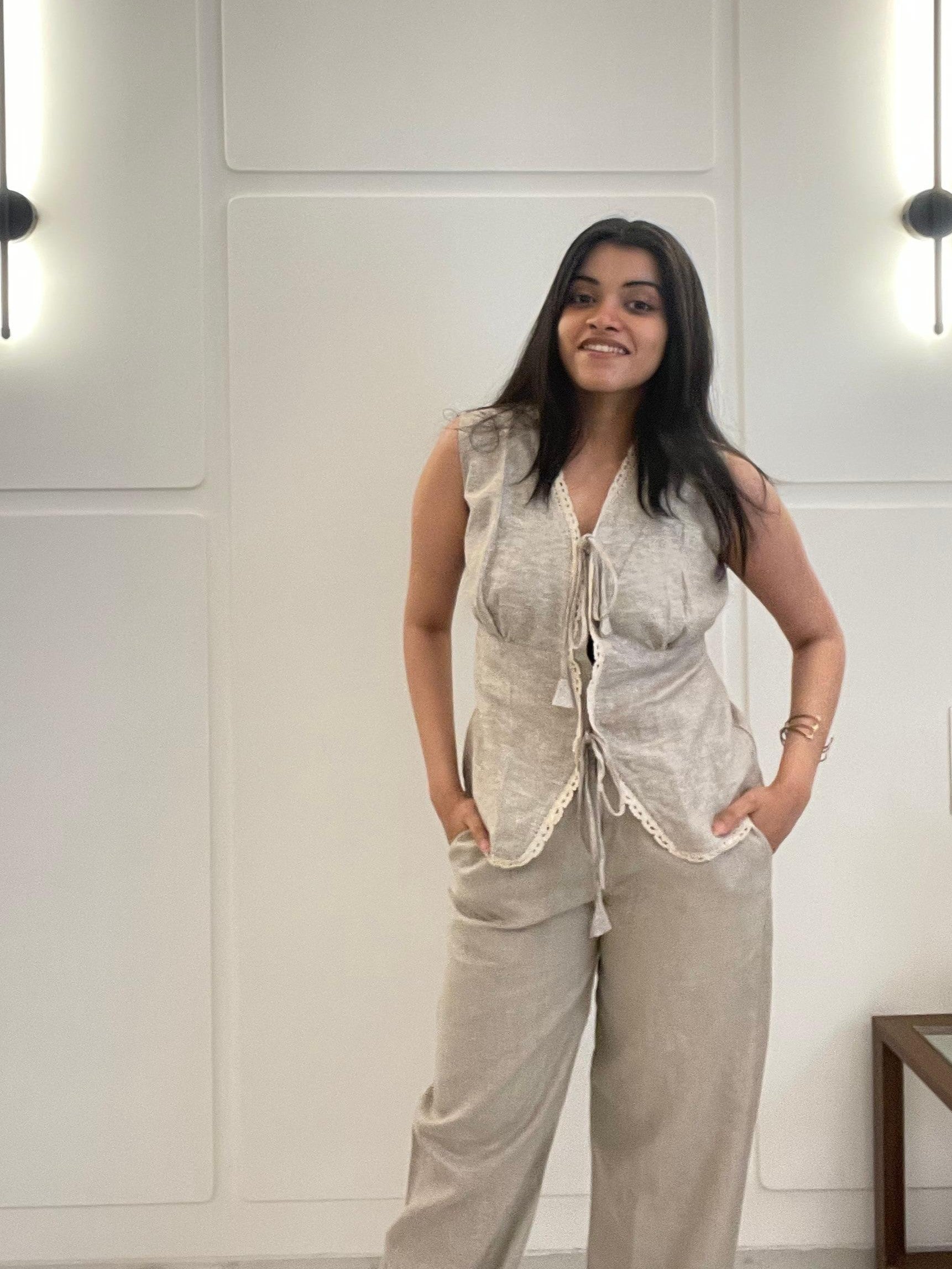 A woman wearing a beige linen waistcoat, sleeveless, and pants in a room with white walls.