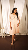 Woman wearing a light pink dress standing in front of white curtains.