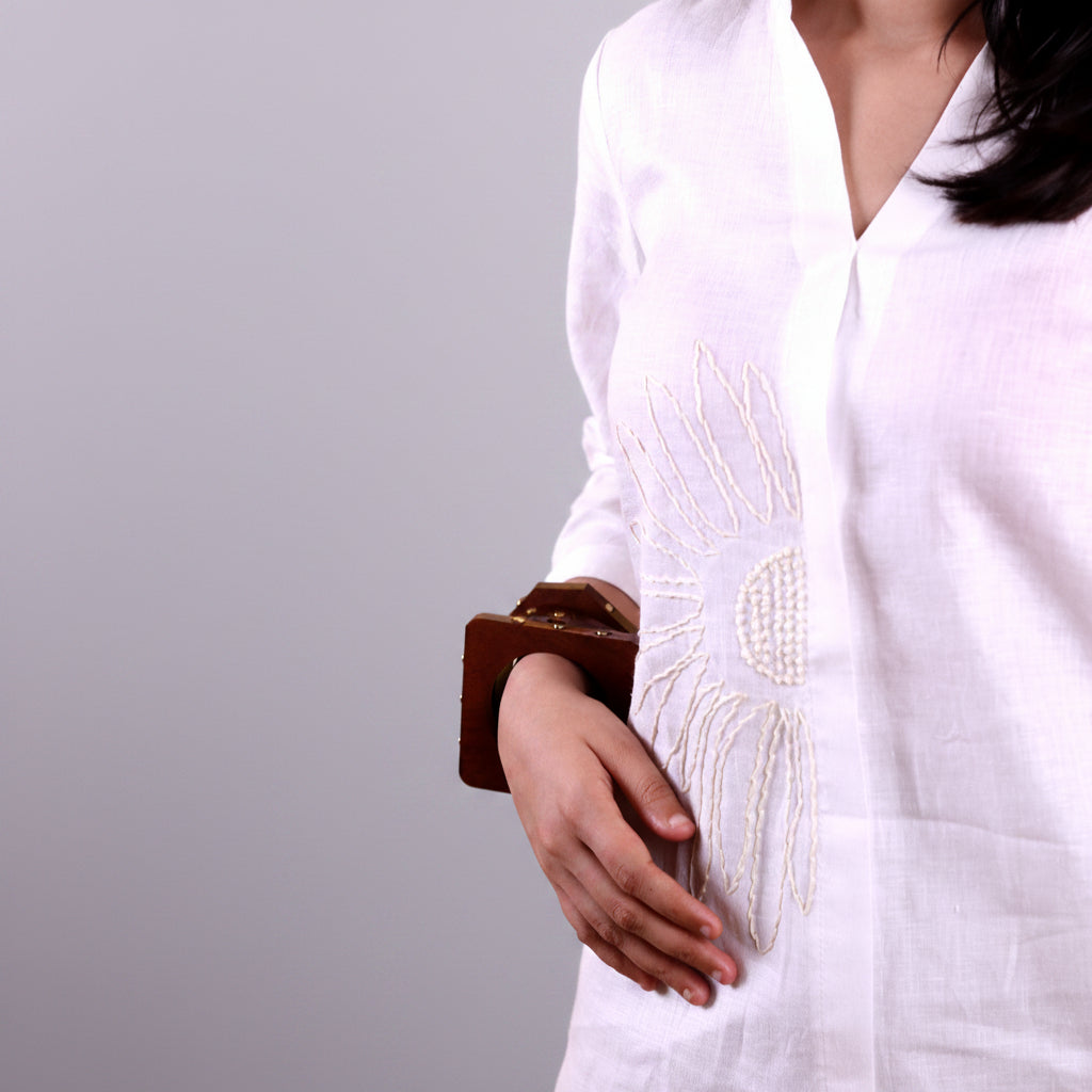Person wearing a white embroidered linen shirt against a yellow background
