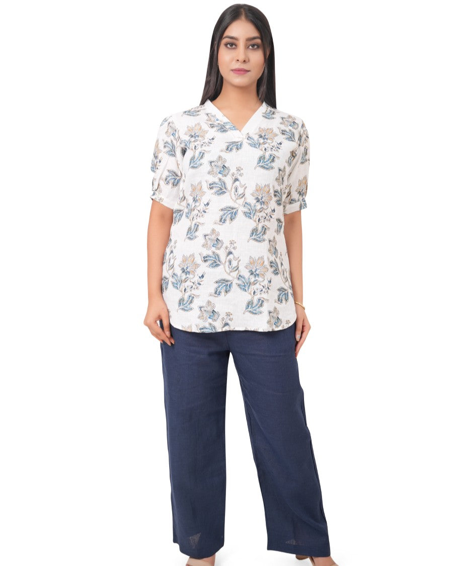 Woman wearing a white floral linen top and navy pants on a white background